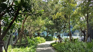 A paved pathway flanked by lush greenery and trees, leading towards a building with a blue facade. - Welcome to the Best and new Apartment to Have Great Trip in Patong Beach (Patong)