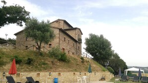 A stone building with a swimming pool, outdoor seating, and a hillside. - Room in Holiday House - Double Twin Room With Balcony Pool View (Monte Castello di Vibio)