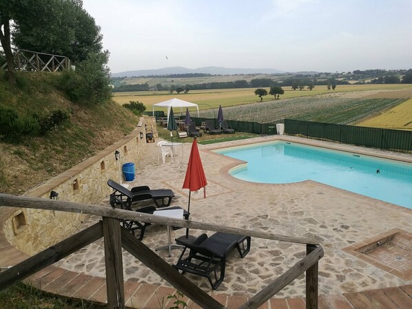 Un área de piscina con suelo de piedra, sillones de descanso y una mesa con sombrillas.