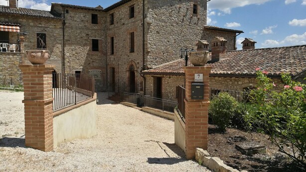A stone building with a traditional architectural style, featuring a courtyard and a gated entrance. - Room in Holiday House - Double Twin Room With Balcony Pool View (Monte Castello di Vibio)