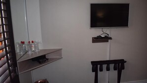 Una habitación con un televisor montado en la pared, un estante pequeño debajo y una silla con una bandeja.