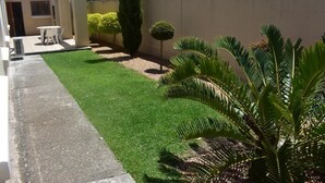 Una propiedad residencial con un césped bien cuidado, un patio con mobiliario exterior y una variedad de plantas, incluyendo una palmera.