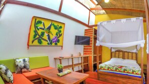 A room with a bed, a sofa, a table, a TV, and a painting on the wall.