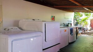 A row of white washing machines under a covered area with a wooden ceiling.