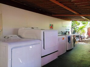 A row of white washing machines under a covered area with a wooden ceiling.