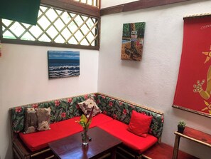 A corner room with a wooden bench, a small table, a wall with a tropical-themed cushion, a framed picture of the ocean, and a red decorative panel. - Villa # 3 - High End Studio Apartment With Kitchen, Playa Chiquita (Cahuita)