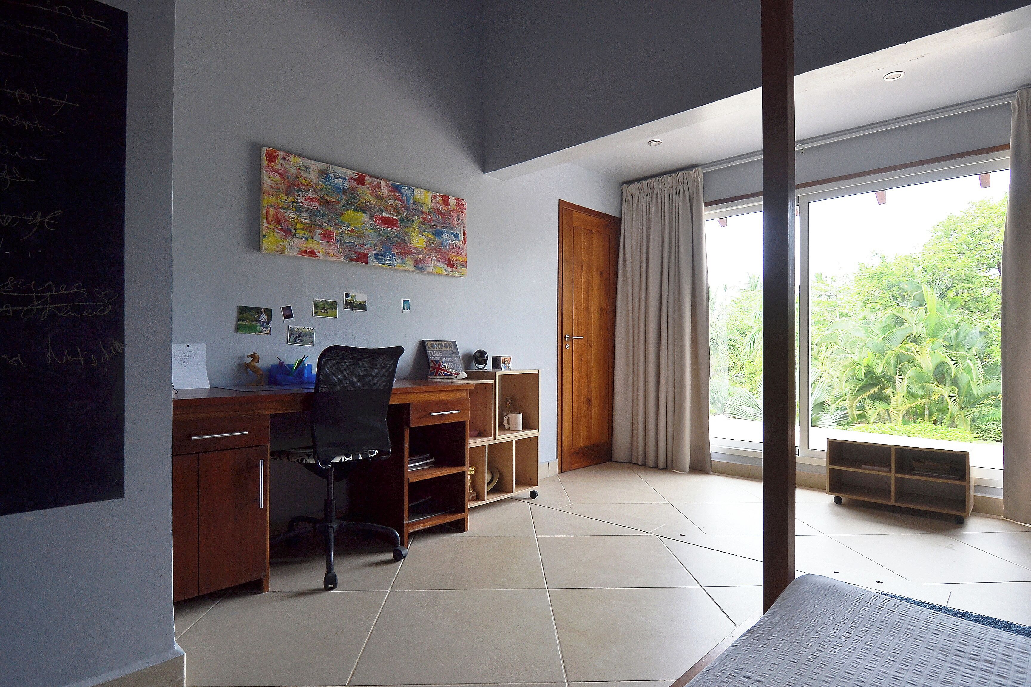 Une pièce comprenant un bureau, une chaise et une grande fenêtre avec des rideaux.