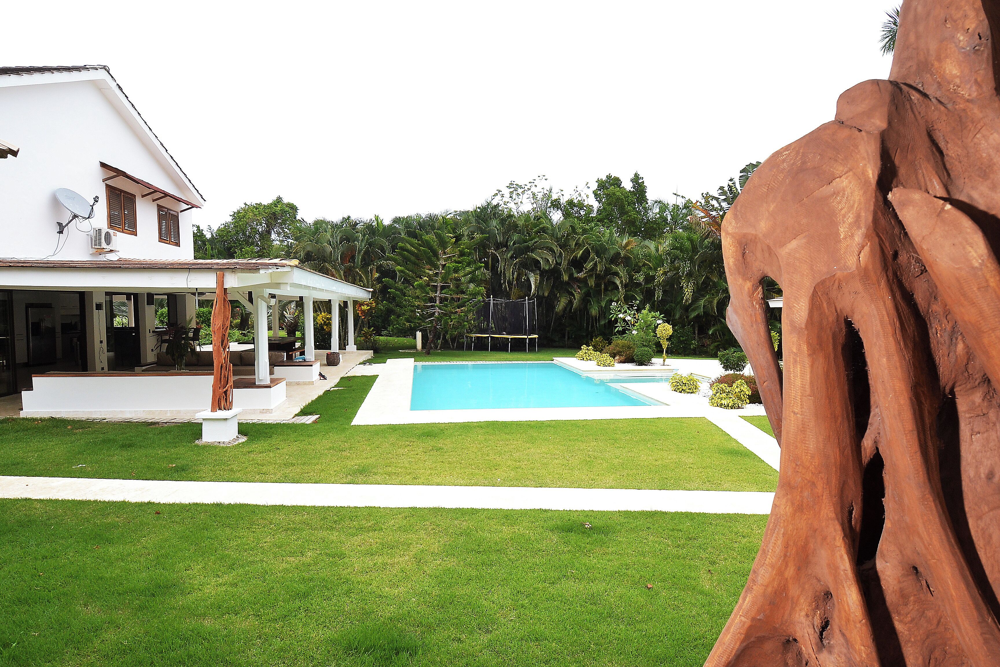 Una casa con piscina, un porche cubierto y un tronco de árbol grande al frente.