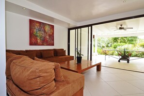 A modern living room with a brown sofa, a coffee table, and a colorful abstract painting on the wall. - Las Terrenas Front Beach And Garden Villa With Private Staff (Las Terrenas)