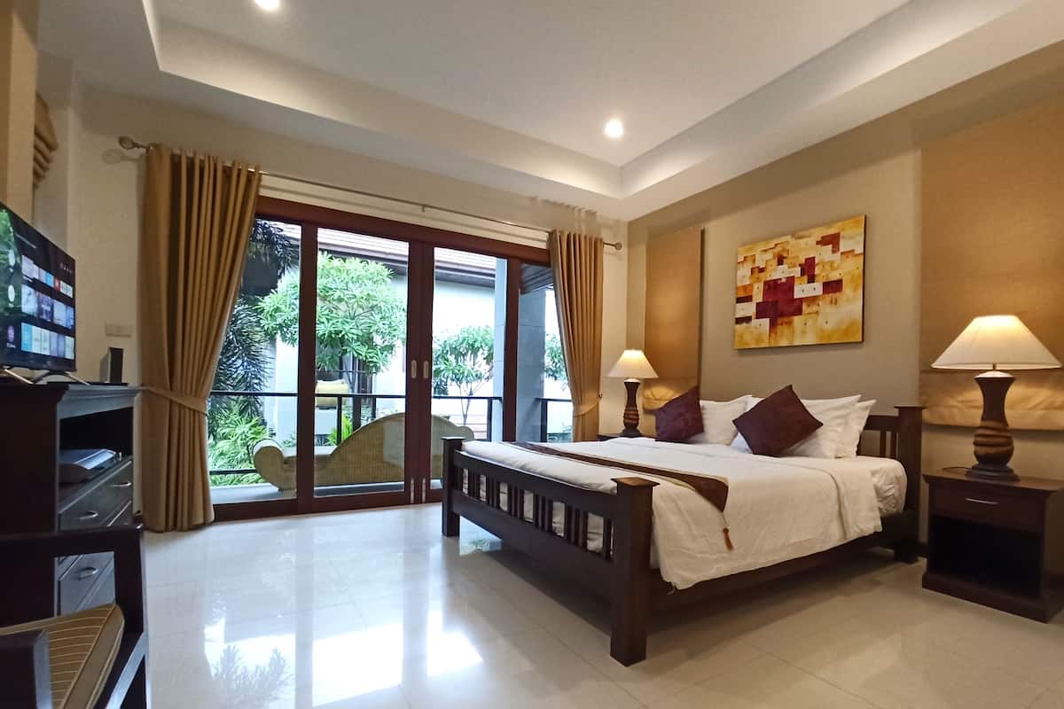 Habitación de hotel con cama, dos lámparas de noche, televisión y balcón con cortinas.
