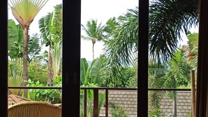 Un balcon agrémenté de meubles en osier, une vue sur une végétation tropicale luxuriante et un mur en briques.