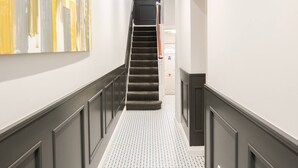 Un couloir doté d’un sol à motifs, d’un escalier et d’un mur orné d’œuvres d’art abstraites.
