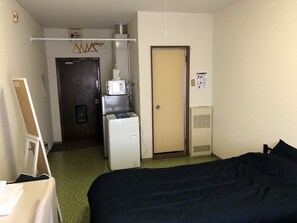 A hotel room with a bed, a microwave, a refrigerator, a door, and a small cabinet. - Nagayama Apartment Twin (Asahikawa)