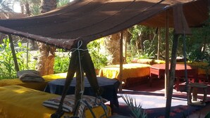 An outdoor seating area with a canopy, tables, chairs, and a hanging light fixture. - Room-auberge Jnane dar Diafa se Trouve a (Tamegroute)