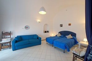 Quarto com sofá azul, cama com roupa de cama azul combinando, mesinha de centro com abajur e luminária na parede.