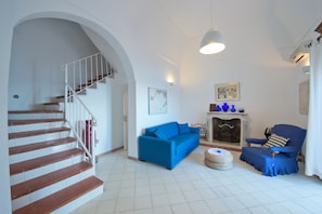 Uma sala de estar com escada, um sofá azul, lareira e uma poltrona azul.