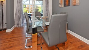 A dining area with a glass table, grey upholstered chairs, and a view through large windows. - Ideal for Alton Towers, Staffordshire and The Peak District (Stoke-on-Trent)