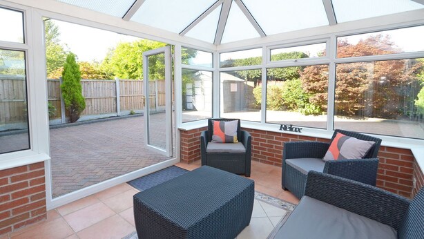 A conservatory with wicker furniture, a glass door, and a view of a garden. - Ideal for Alton Towers, Staffordshire and The Peak District (Stoke-on-Trent)