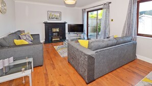 A living room with grey sofas, a fireplace, a TV, and a glass table. - Ideal for Alton Towers, Staffordshire and The Peak District (Stoke-on-Trent)