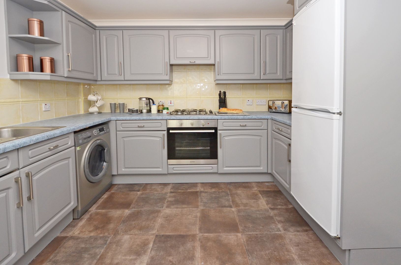 A kitchen with grey cabinets, a washing machine, an oven, and a refrigerator.