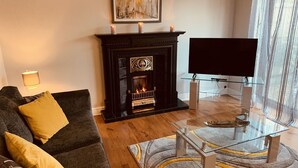 A living room with a fireplace, a sofa, a glass coffee table, and a flat-screen TV. - Ideal for Alton Towers, Staffordshire and The Peak District (Stoke-on-Trent)