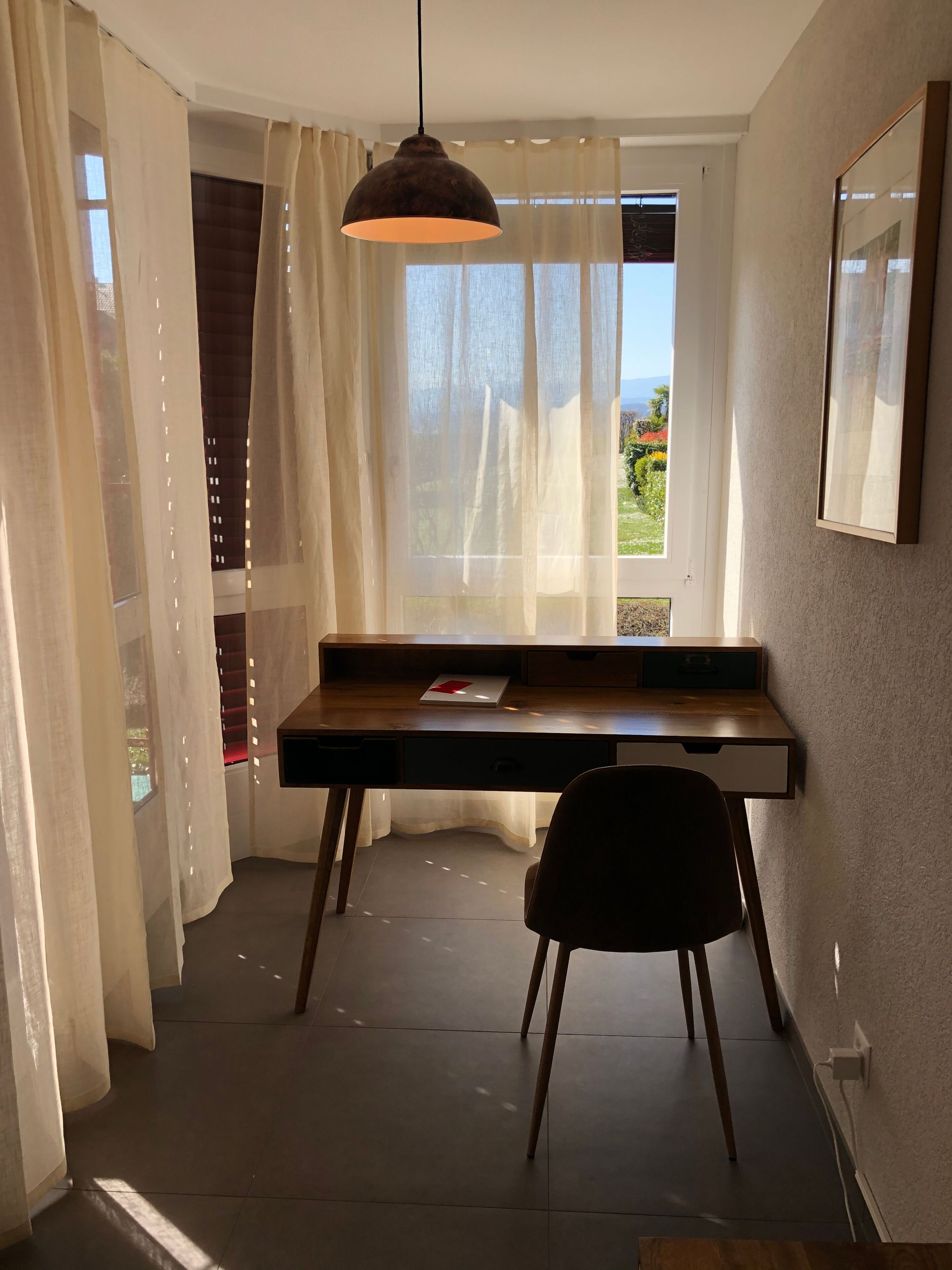 A room with a desk, chair, and a hanging light fixture.