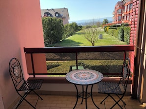 A balcony with two metal chairs and a small round table, overlooking a well-maintained garden and a distant building. - Amazing Studio In Lausanne Close To Epfl and Unil (Ecublens)