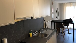 A modern kitchen with white cabinets, a black marble backsplash, a stainless steel sink, and a small bar area with stools. - Amazing Studio In Lausanne Close To Epfl and Unil (Ecublens)