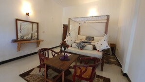 A bedroom with a canopy bed, a bedside table, a chair, a mirror, and a wall-mounted shelf. - Mbv Hotel Annex Standard Bungalow (Matemwe)