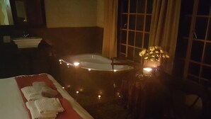 Una habitación tenuemente iluminada con una cama, una mesita con una vela y una bañera con luces.