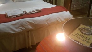 Una cama bien hecha con sábanas blancas y una manta roja, una mesita con una lámpara y una pared con un diseño decorativo.
