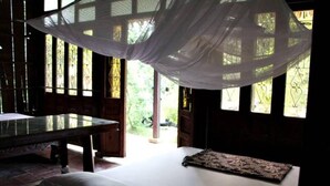 Una habitación con una cama, una mesa y un banco. Se observan ventanas con detalles de hierro decorativo.