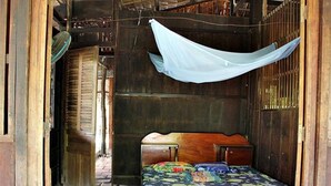 A wooden room with a bed, a fan, and a hanging cloth.