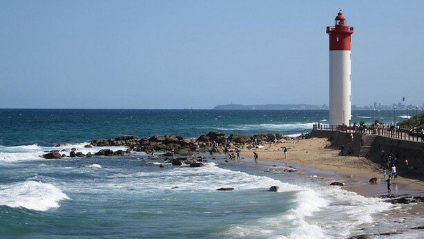 Un phare se dresse sur une plage rocheuse, tandis que les vagues déferlent sur le rivage.
