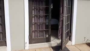 Une porte d’entrée avec un grillage métallique donnant sur une pièce où se trouve un lit.