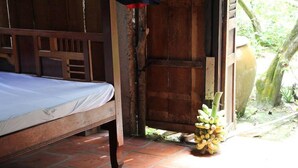 Una cama de madera en una habitación con suelo de baldosas y una puerta que da al exterior.
