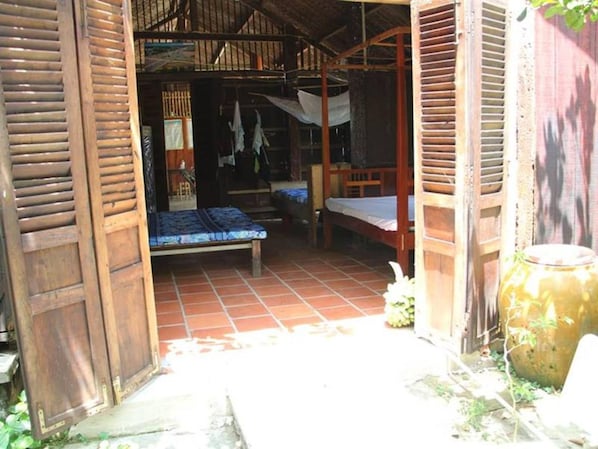 A rustic wooden structure with two beds, a tiled floor, and a large pot.