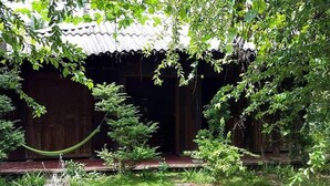 Una casa de madera tradicional con techo de tejas, rodeada de abundante vegetación y plantas en macetas.