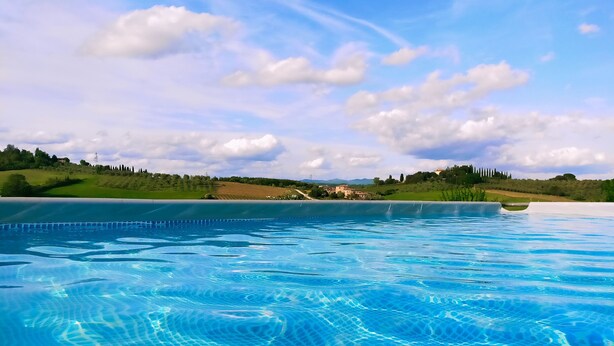 A clear swimming pool with a view of a green landscape and distant buildings. - Villa Degli Olivi Siena (Siena)
