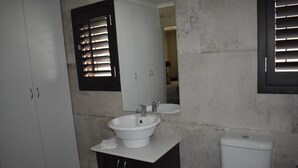 Un baño con lavamanos blanco, mueble oscuro y un inodoro.