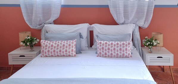A bed with two pillows, a bedside table with a vase, and a wall with curtains.