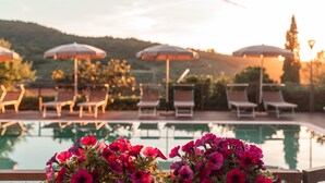 Un espace aménagé au bord de la piscine, avec des chaises longues et des parasols, entouré de collines.