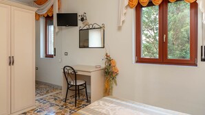 Une chambre à coucher comprenant un lit, un bureau, une chaise, une armoire, un téléviseur et une fenêtre avec des rideaux.