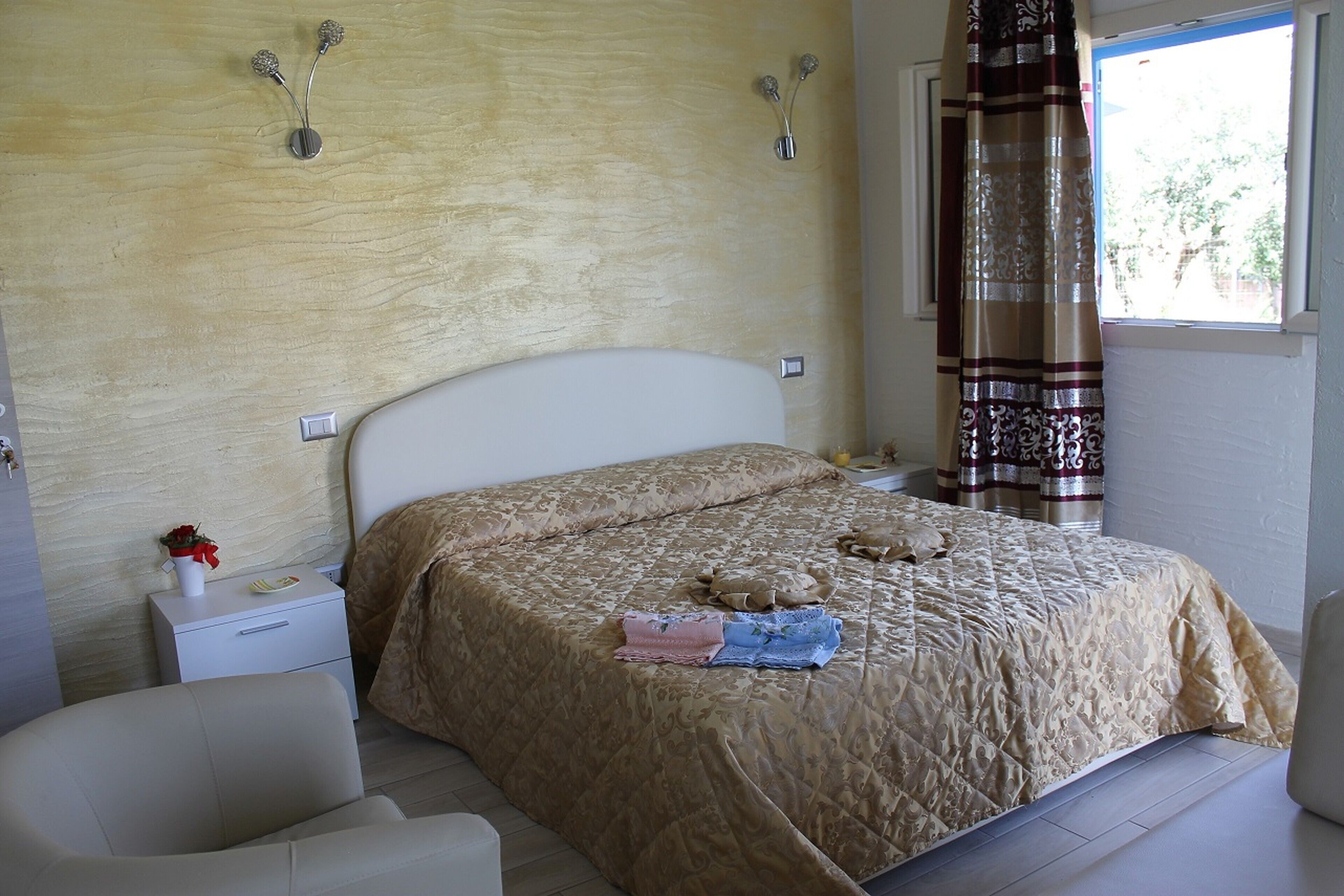 Een slaapkamer met een bed, nachtkastjes, een stoel en een raam met gordijnen.