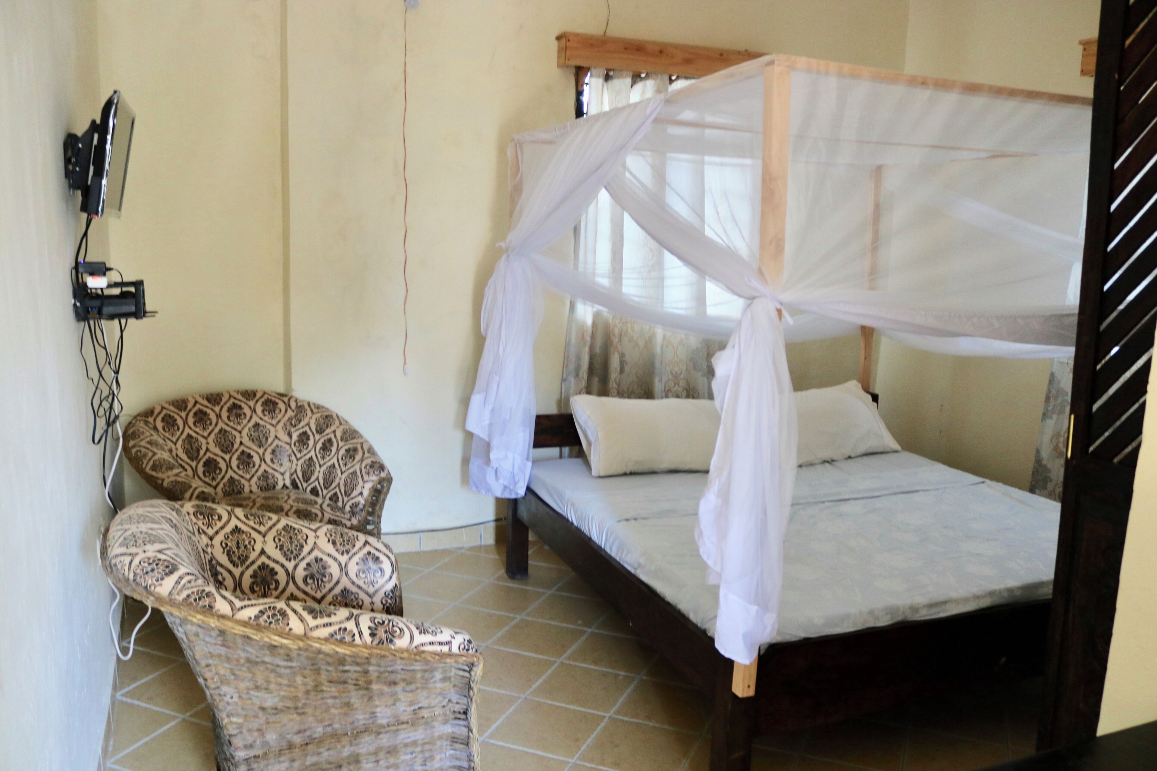A room with a bed with a mosquito net, a wicker chair, and a wall-mounted telephone.