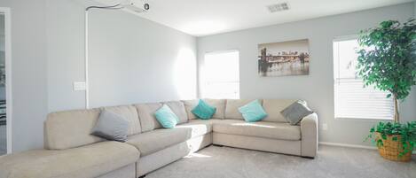 A living room with a beige sectional sofa, a large window, and a plant.