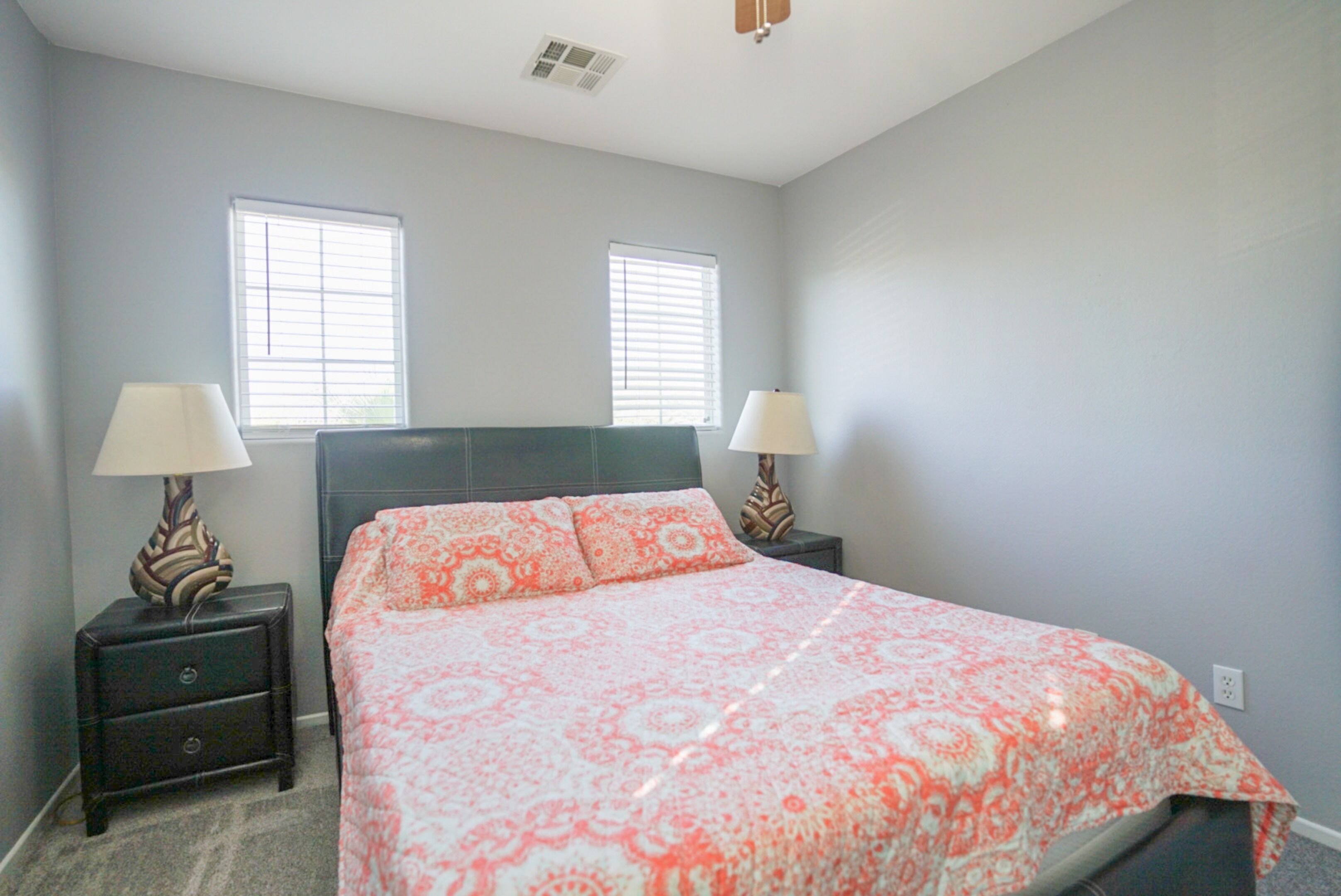 A bedroom with a bed, two nightstands, two lamps, and two windows.