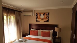 A hotel room with a large bed, a nightstand with a lamp, an air conditioning unit, and a painting on the wall. - Fairview Bed And Breakfast - Double Bedroom 5 (Umhlanga)
