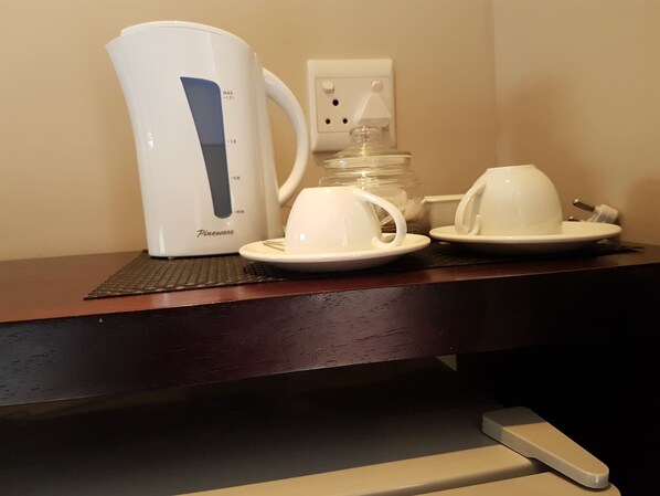Une machine à café, deux tasses et un bocal sur une surface en bois.