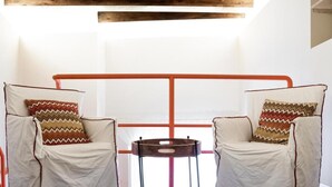 Una habitación con dos sillas, cada una con un cojín estampado, una mesita redonda pequeña y una viga de madera en el techo.